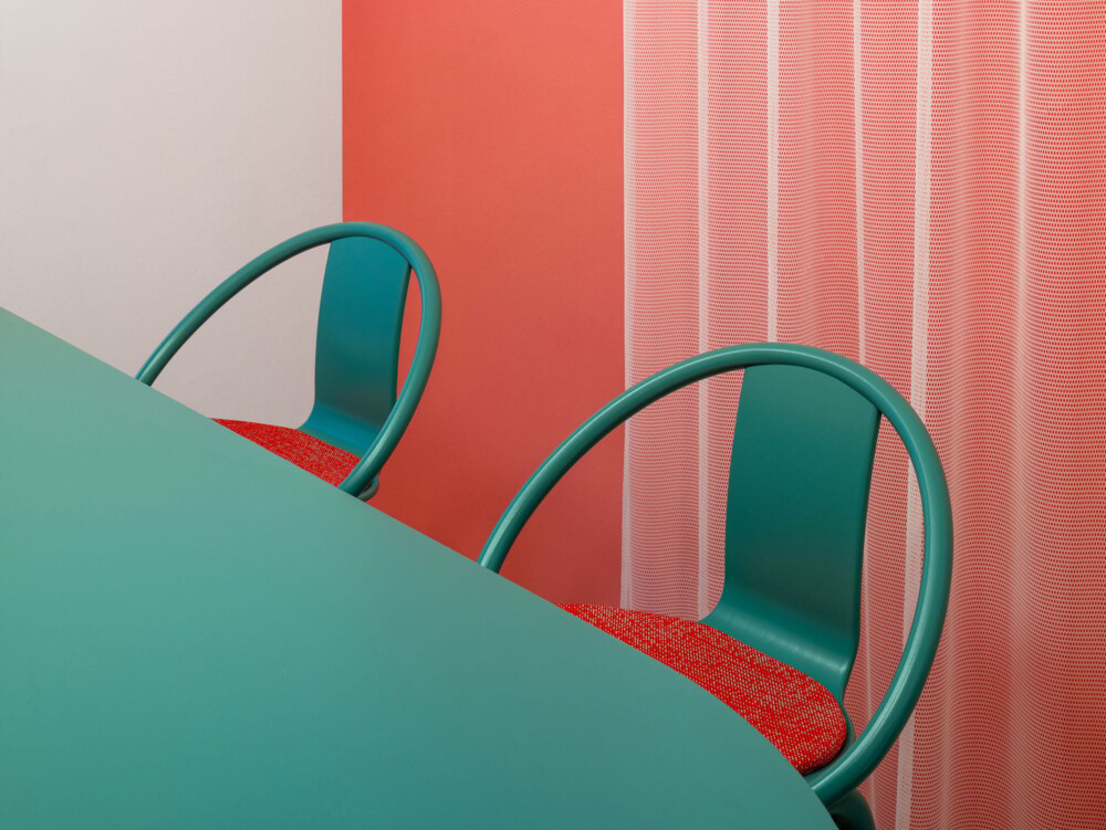 Farbkonzept Café Stuttgart: Gezielt eingesetzte Türkis-Akzente auf Korallen-Hintergrund. Die abgerundete Formgebung der Stühle und Tische im Gastro-Ladenbau schafft ein einladendes und verspieltes Ambiente