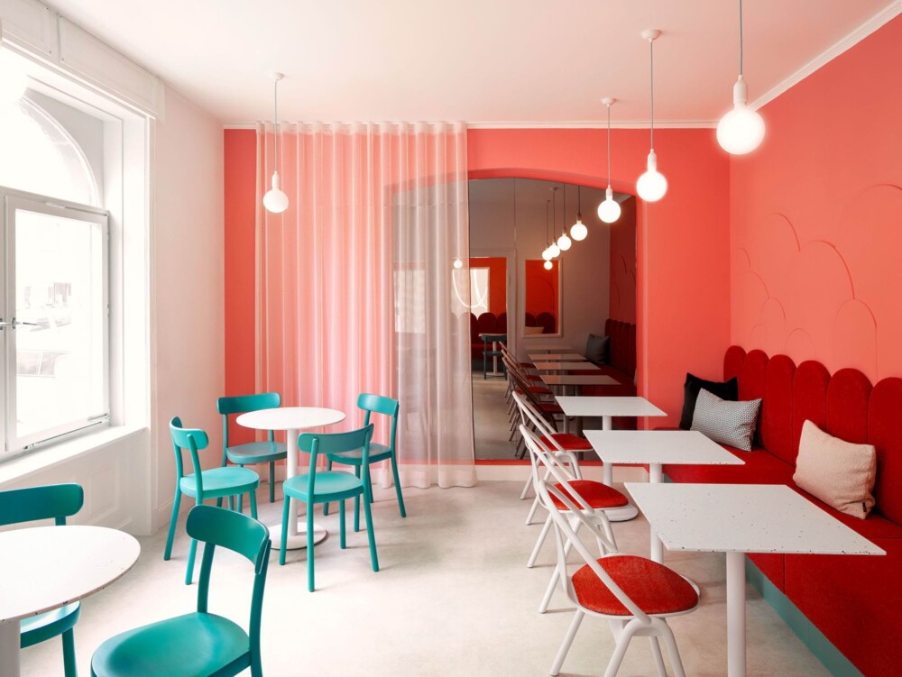 Raumgestaltung mit Durchblick: Architektonisch betonte Bögen schaffen eine optische Trennung der Gasträume. Die Innenarchitektur nutzt hohe Decken und weiße Fensterrahmen, um die Intensität der Farben auszubalancieren und Licht zu maximieren